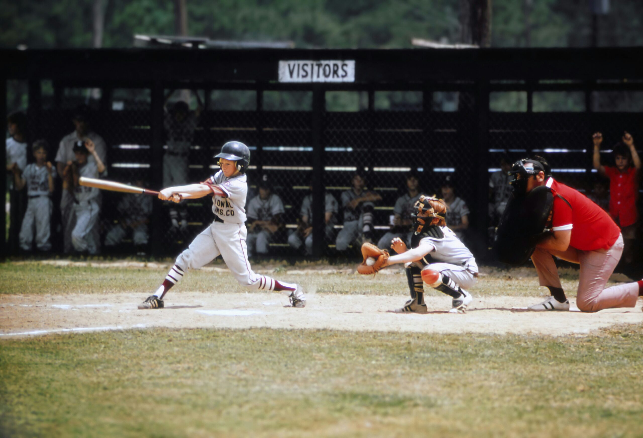 A baseball player swings at a pitch while the catcher receives the ball and the umpire watches from behind home plate.