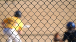 A baseball player can be seen at bat through a chain-link fence.