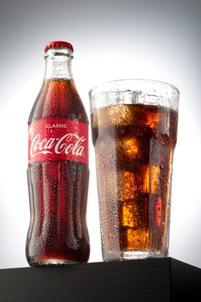 Coca-Cola glass bottle beside a glass of cola with ice.