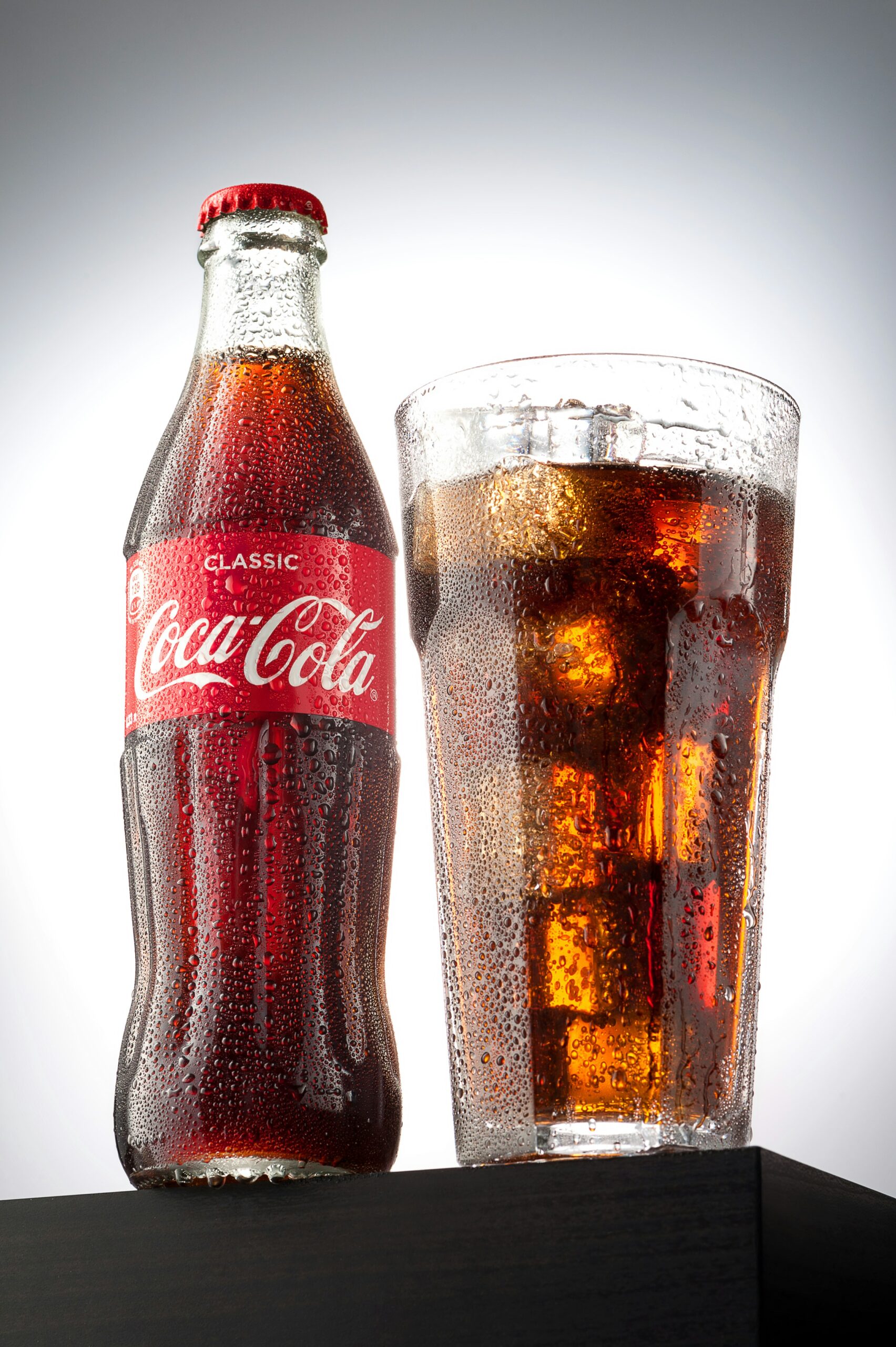 Coca-Cola glass bottle beside a glass of cola with ice.