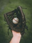 A hand in a baseball glove, holding a baseball.