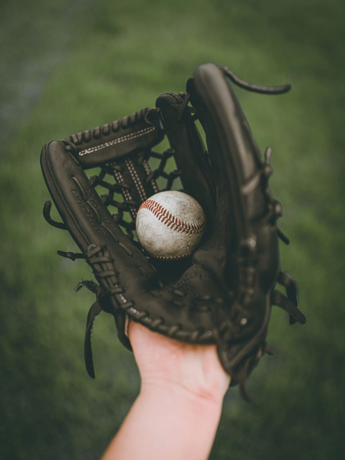 A hand in a baseball glove, holding a baseball.