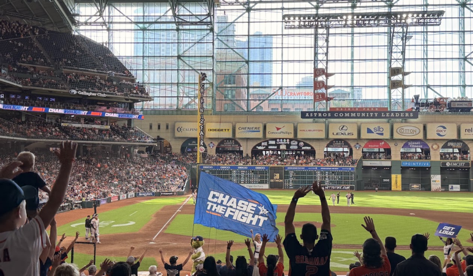 Astros mascot Orbit carries the "Chase the Fight" flag as fans cheer during a game at Daikin Park.