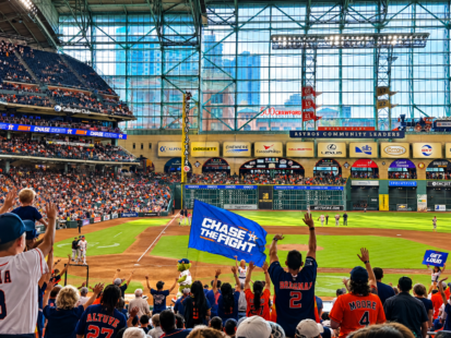 Astros fans cheer at Daikin Park as a “Chase the Fight” flag waves over the crowd during a game.