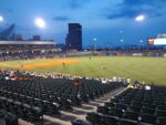 Baseball players on the field during an evening game at a minor league ballpark.