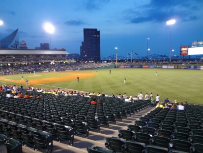 Baseball players on the field during an evening game at a minor league ballpark.