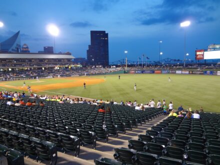 Baseball players on the field during an evening game at a minor league ballpark.