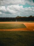 Baseball players stand on a field beneath dark clouds gathering overhead.