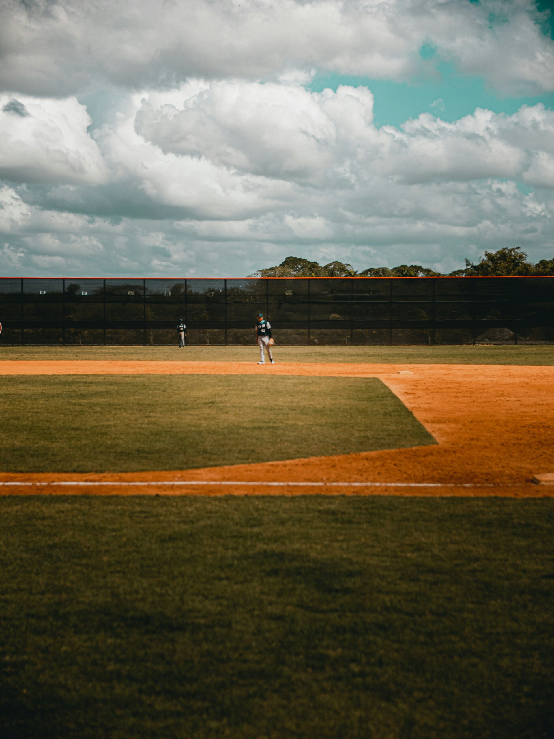 Baseball players stand on a field beneath dark clouds gathering overhead.