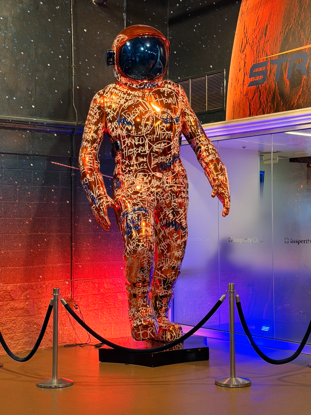 Astros astronaut statue covered in signatures and illuminated by orange and blue lights at Daikin Park.
