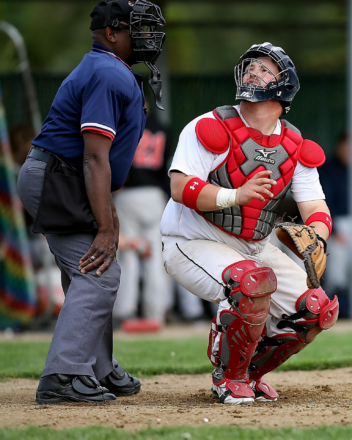 Catcher in red protective gear looks back at the home plate umpire during a baseball game.