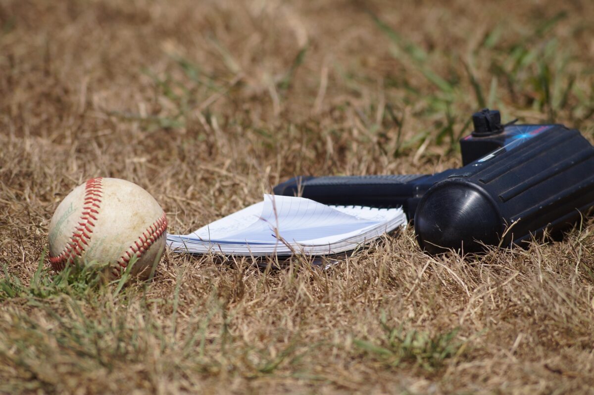 Baseball, scouting notebook, and radar gun on the grass.