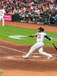 Nelson Velázquez follows through on a swing for the Astros at Daikin Park as photographers and fans watch from behind home plate.