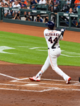 Yordan Alvarez follows through on a swing at Daikin Park as photographers and fans watch from behind home plate.