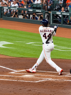Yordan Alvarez follows through on a swing at Daikin Park as photographers and fans watch from behind home plate.
