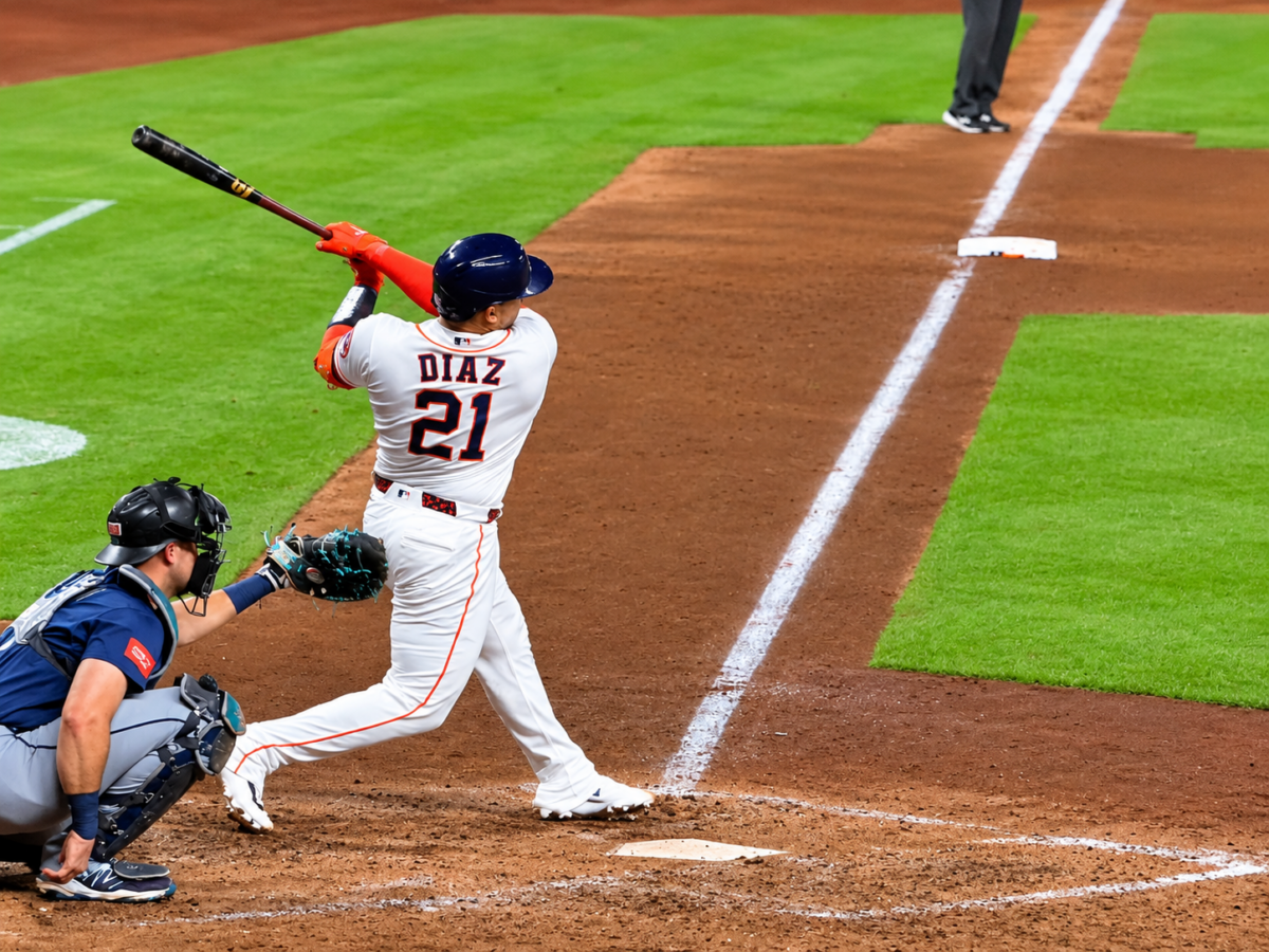 Houston Astros catcher Yainer Díaz follows through on a swing at Daikin Park, wearing his white No. 21 uniform as the opposing catcher crouches behind home plate.
